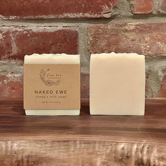 Two bars of unscented and uncolored sheep's milk soap on a wooden board with a brick background