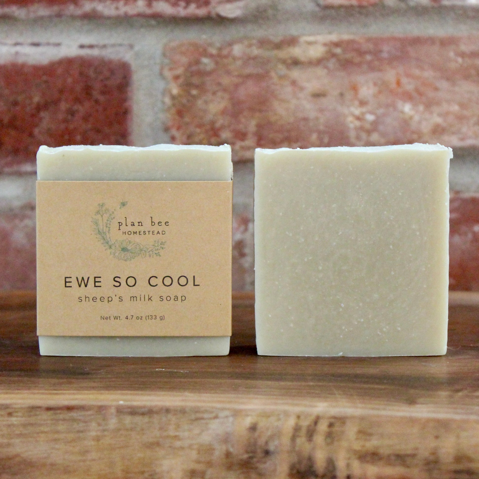 Two bars of cucumber mint sheep's milk soap on a wood board with brick background.