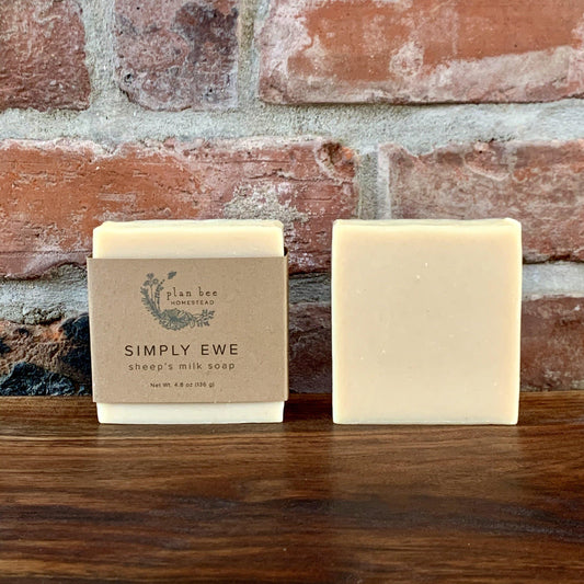 Two bars of Simply Ewe Sheep's Milk Soap on a wooden board with a brick background.